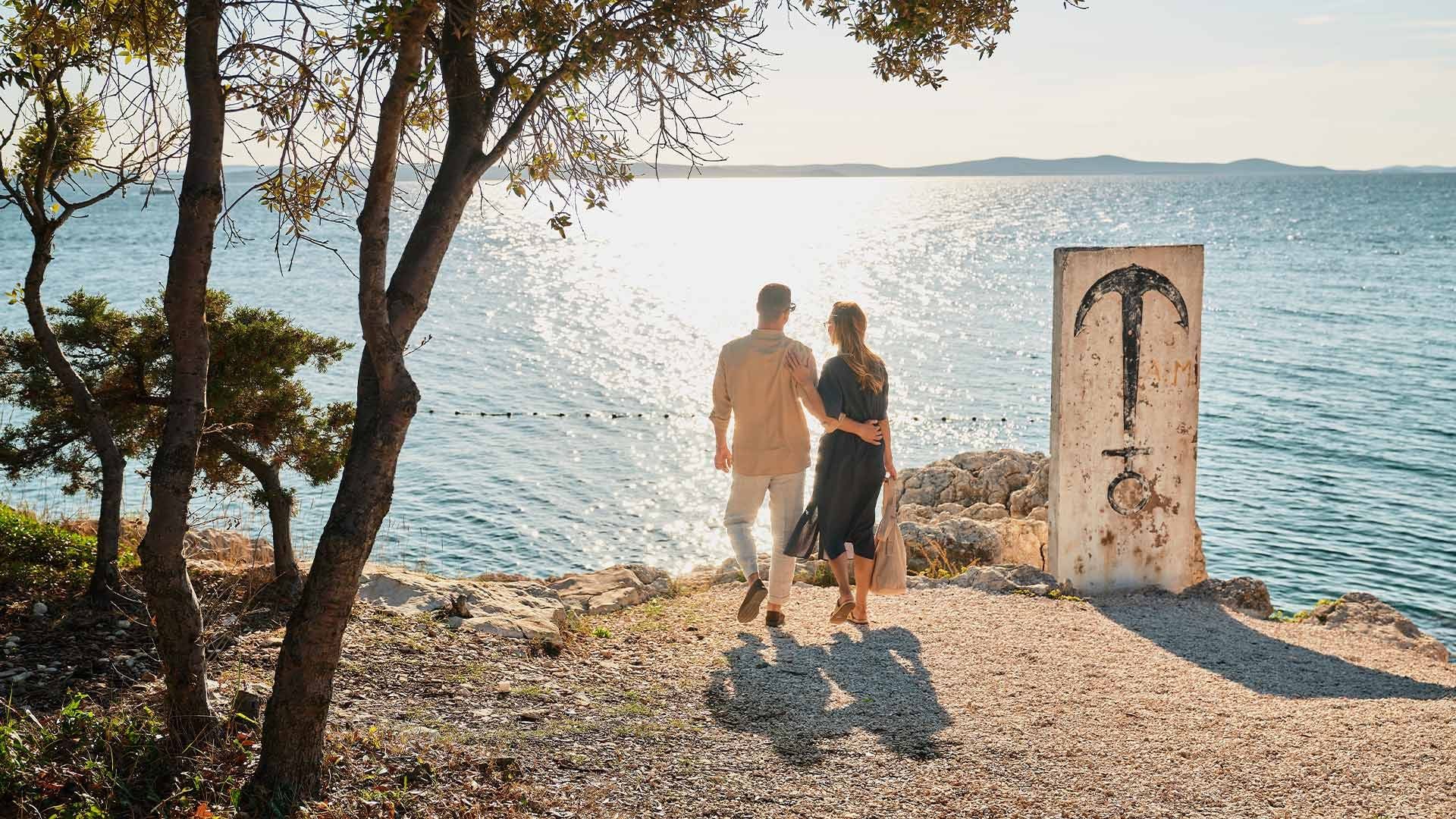 Couple walking hand in hand near the sea with a white sign with a hammer design.
