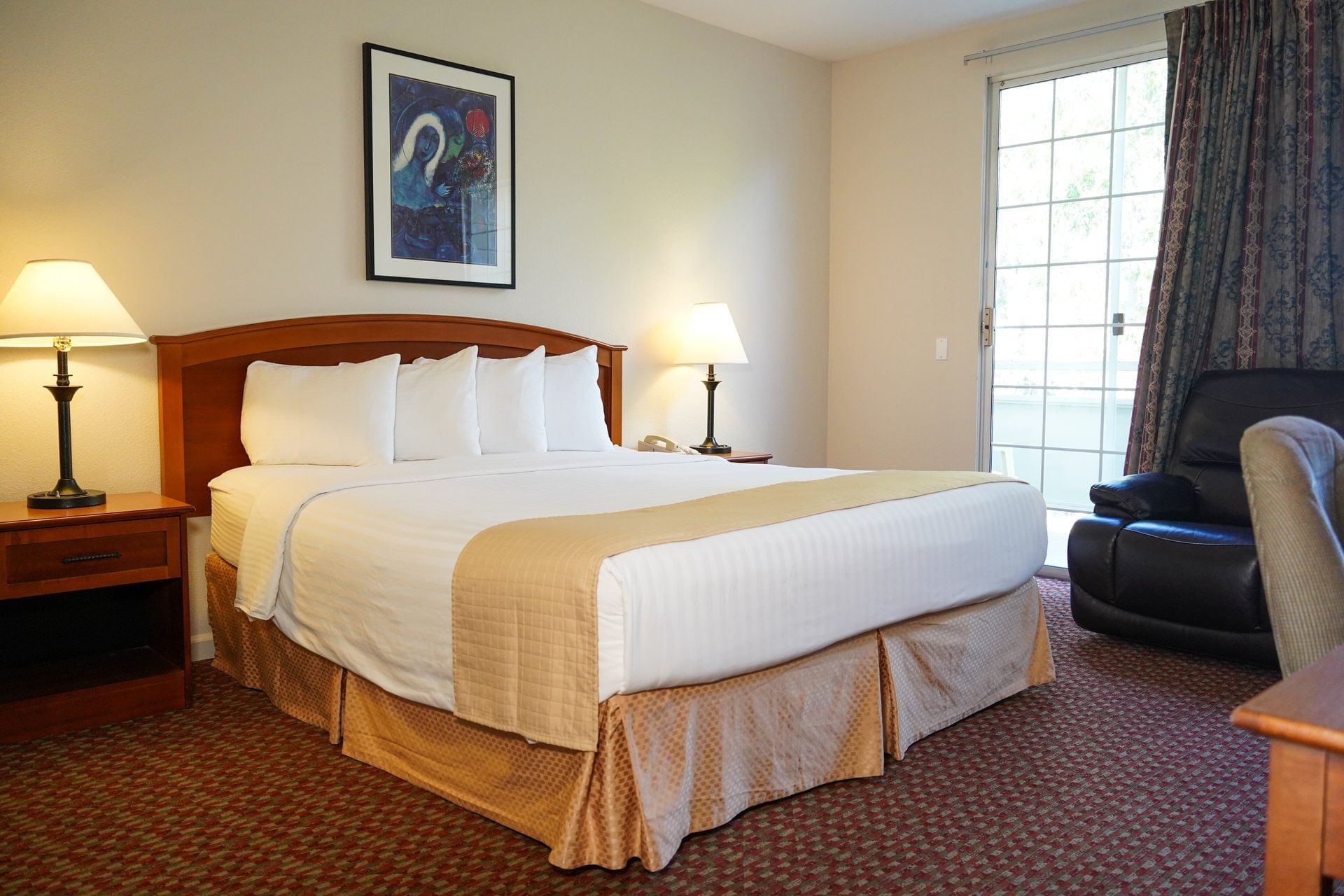 A standard hotel room with a large bed, wooden furniture, and a door leading outside.