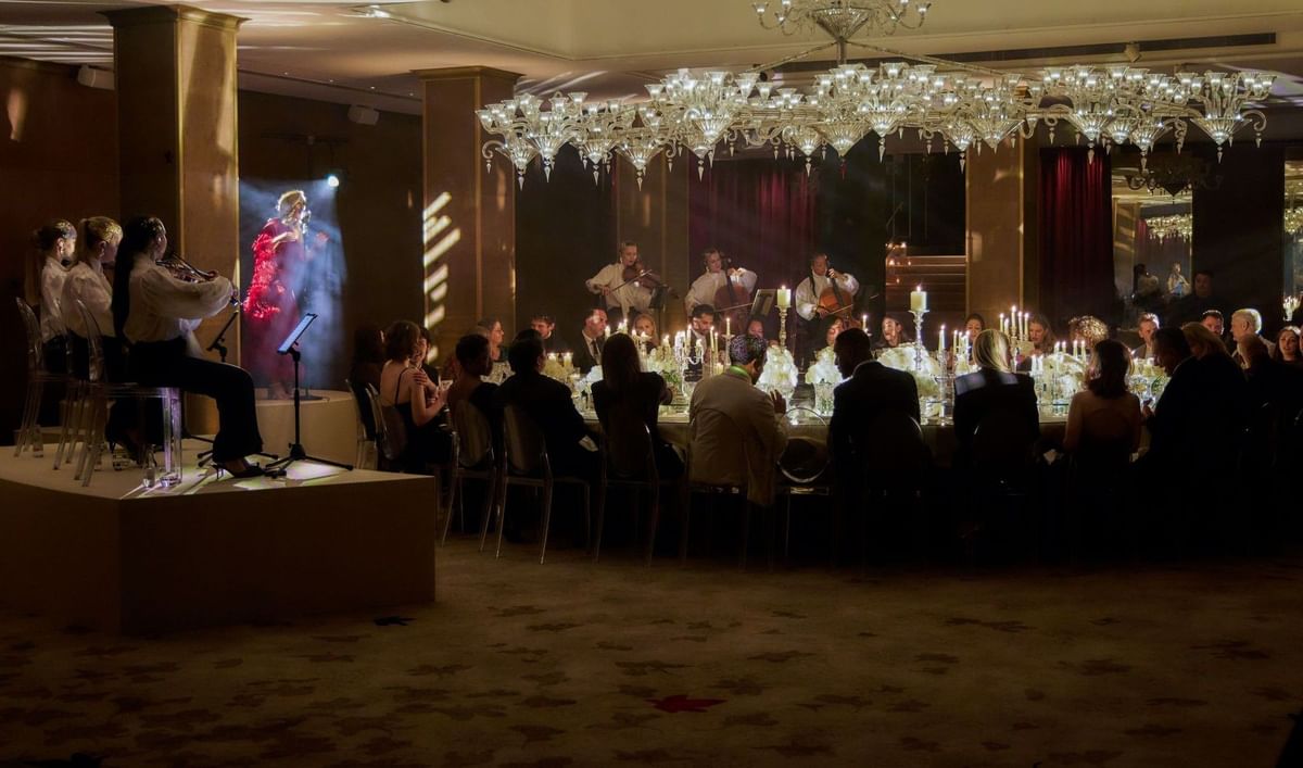 Guests dining under crystal chandeliers with live music at The May Fair Hotel, London.