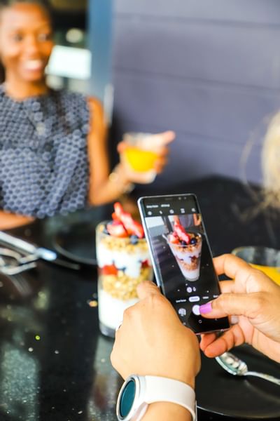 A hand holding a smartphone captures a parfait dessert at Riverside Hotel Fort Lauderdale