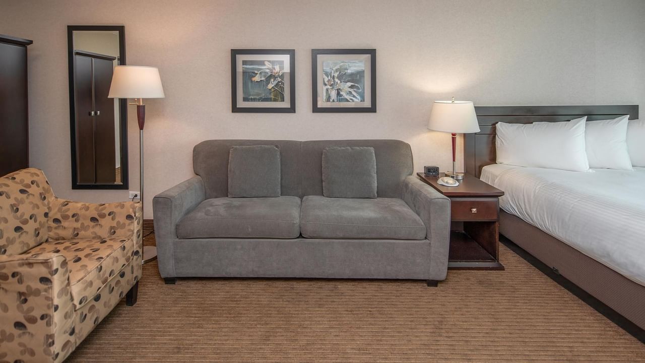 Hotel suite with a queen bed, sofa, armchair and bedside lamps.