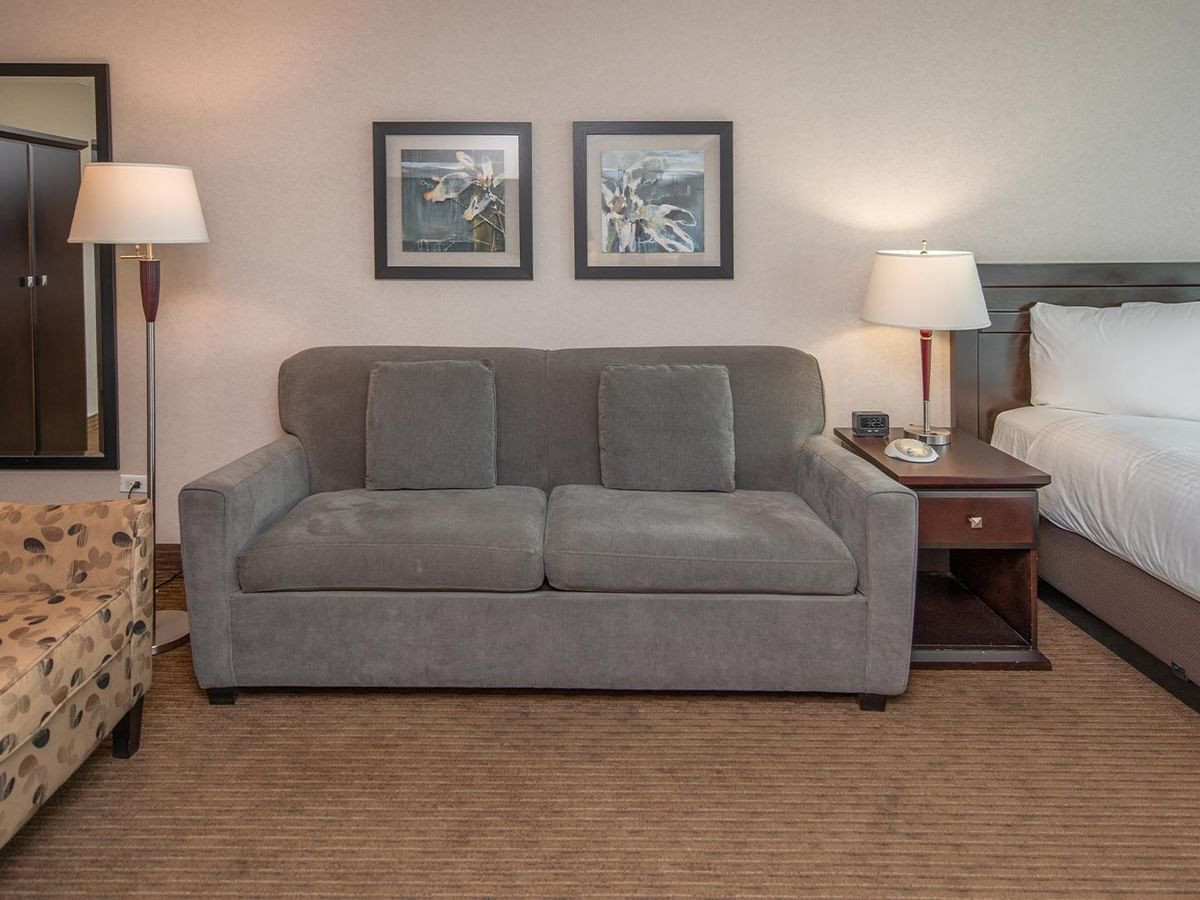 Hotel guest room with a queen bed, sofa, armchair and bedside lamps.