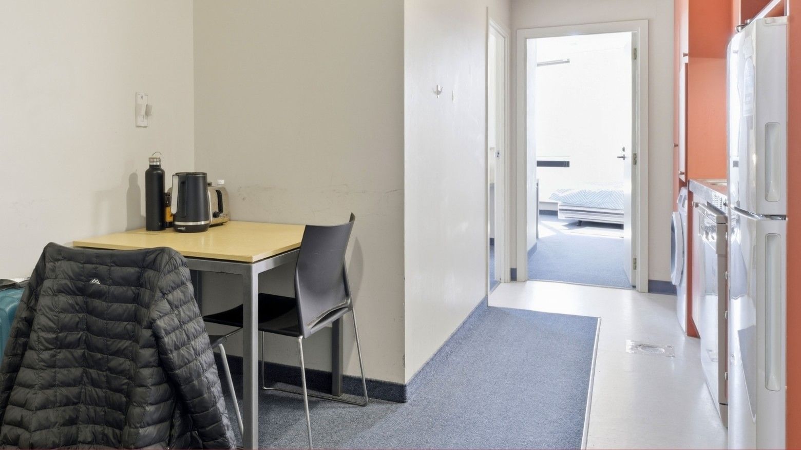 Clean and modern room with a small table, refrigerator, and open door at UniLodge Stafford House.