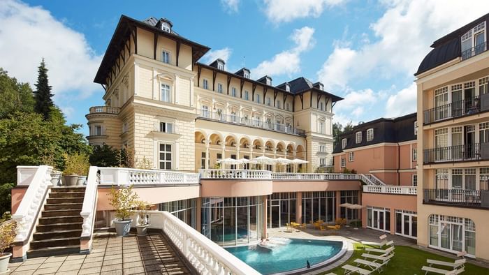 Elegantes Hotelgebäude mit Pool, Terrasse und Liegestühlen im Außenbereich unter blauem Himmel.