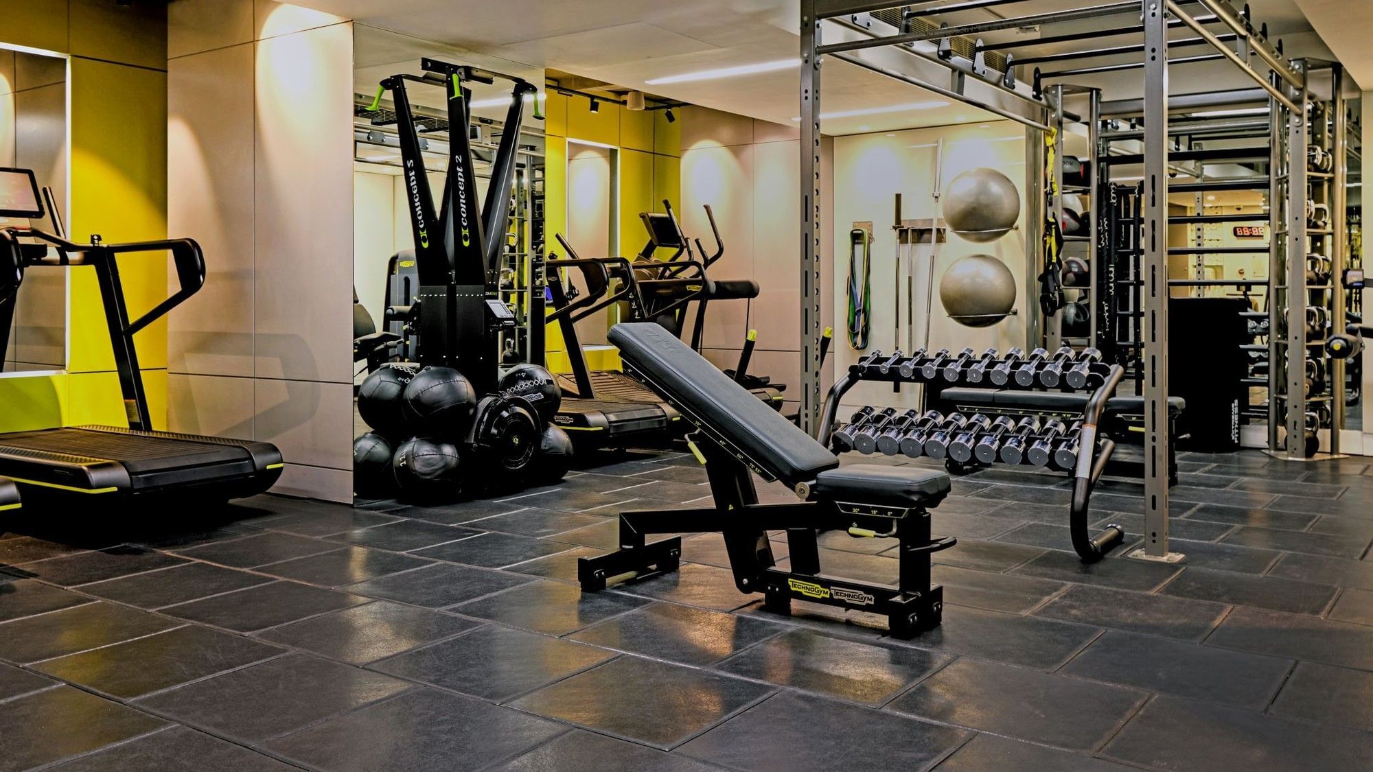 Modern gym with various equipment and black tiled floor at The May Fair Hotel.