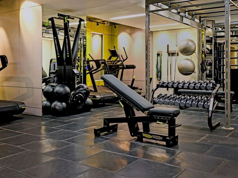 Modern gym with various equipment and black tiled floor at The May Fair Hotel.