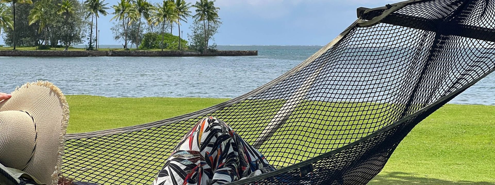 Guest in pattern pants by the water under cloudy skies on a black hammock