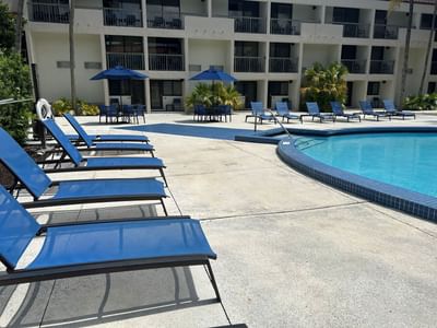 Blue sun loungers beside the outdoor pool and shaded tables beneath an umbrella in the courtyard at Miami Lakes Hotel
