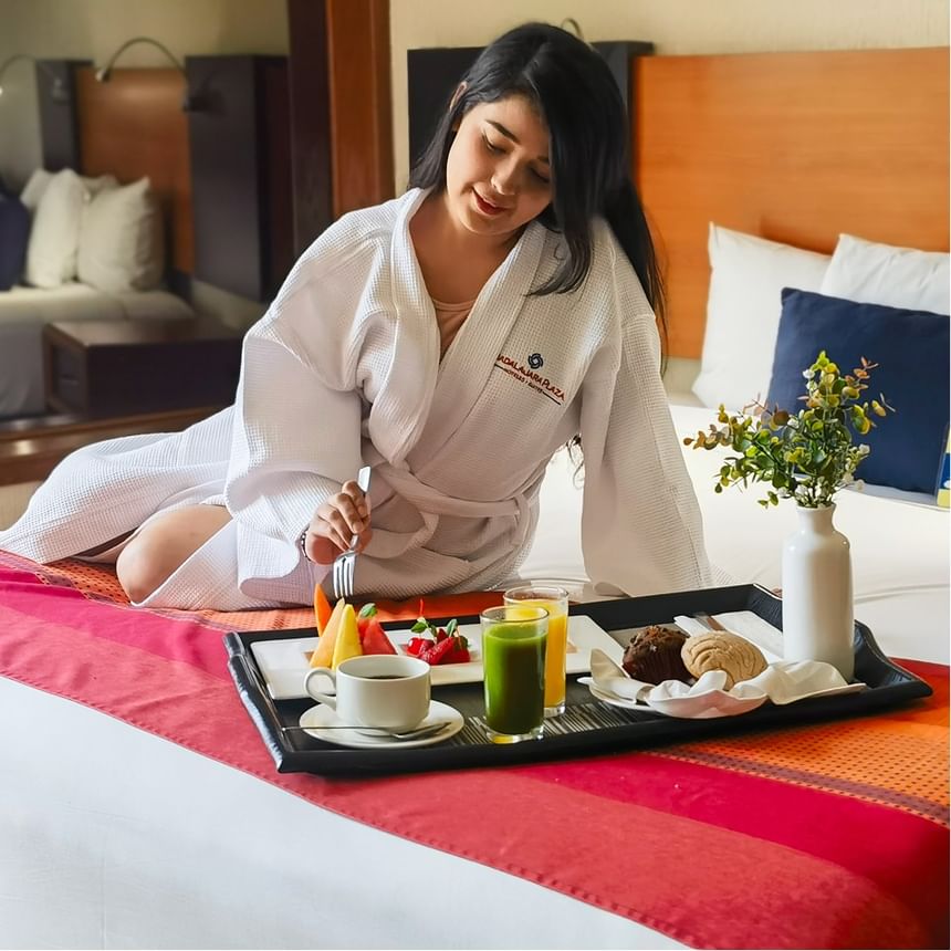 Mujer en bata de hotel disfrutando desayuno en la cama en Hotel Guadalajara Plaza Expo