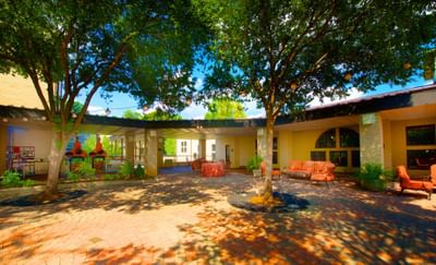 The sunlit outdoor courtyard at the Bolger Center, featuring a covered patio with tables, seating, and a large tree