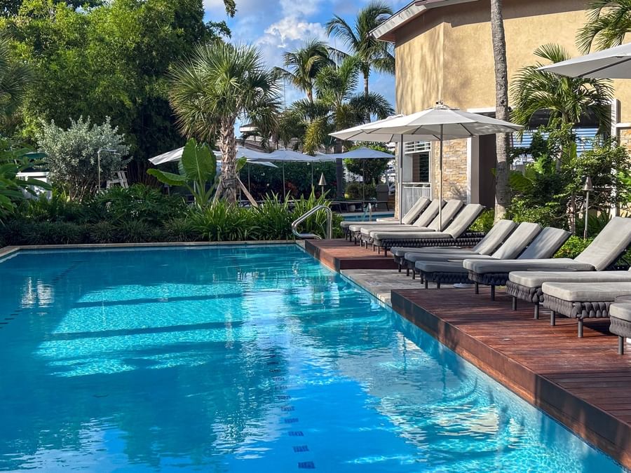 Grey loungers by a clear pool under white umbrellas surrounding lush plants at Warwick Paradise Island Bahamas