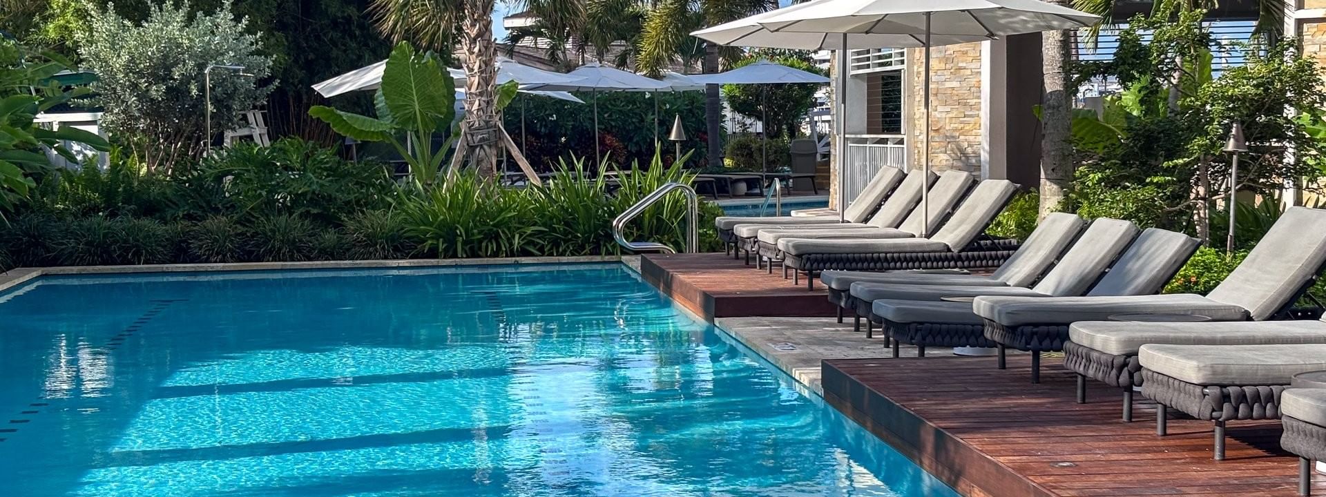 Grey loungers by a clear pool under white umbrellas surrounding lush plants at Warwick Paradise Island Bahamas