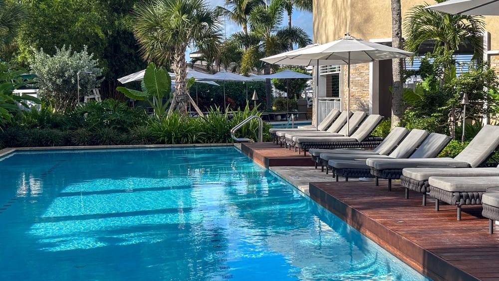 Grey loungers by a clear pool under white umbrellas surrounding lush plants at Warwick Paradise Island Bahamas