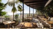 Open-air beachfront restaurant with panoramic ocean views, natural textures, and relaxed seating.