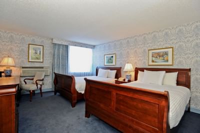Two wooden sleigh beds near window in the guest room with patterned wallpaper at Farmington Inn and Suites