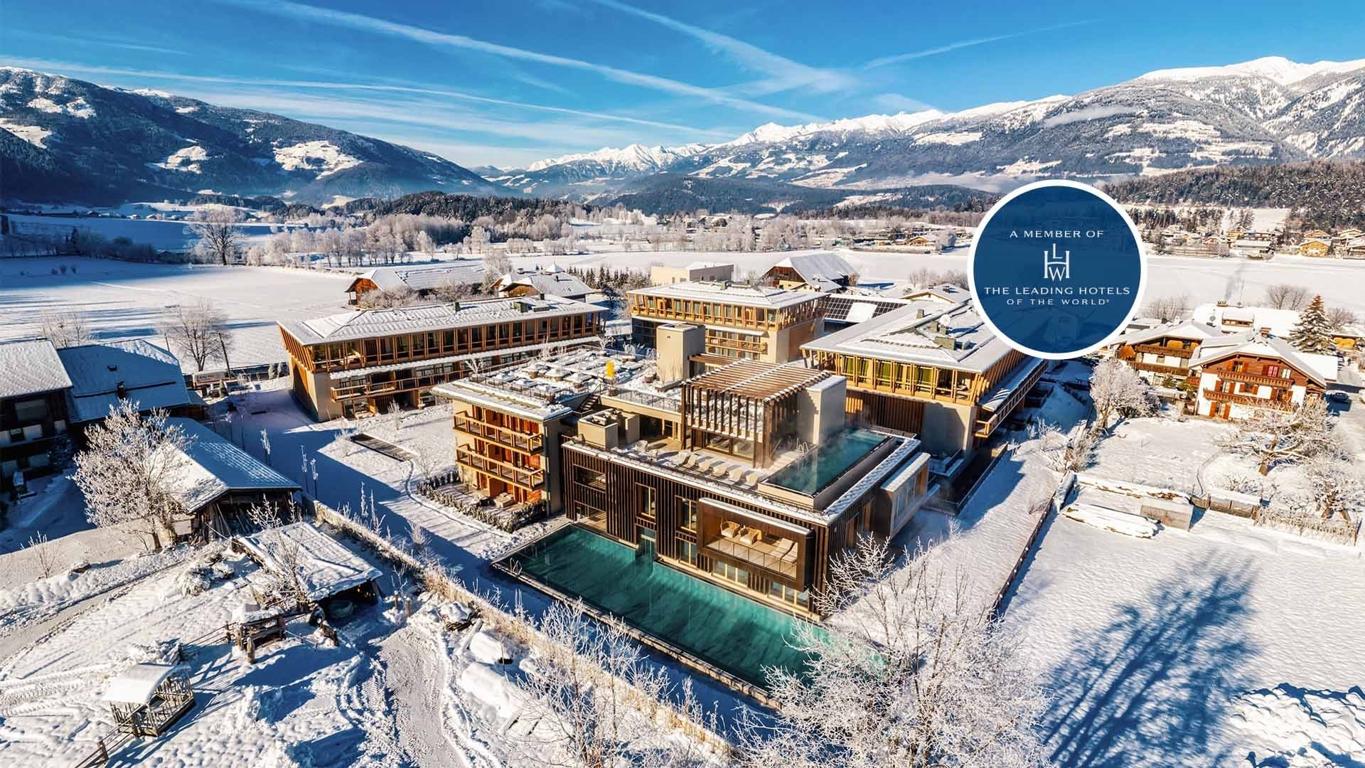 Luftaufnahme eines modernen Hotels in den Alpen mit Pool und schneebedeckter Umgebung.