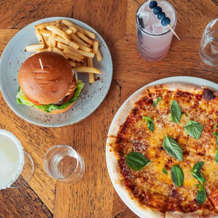 A table with a burger and fries, pizza, and assorted drinks in Karinyas Restaurant at Mercure Kooindah Waters