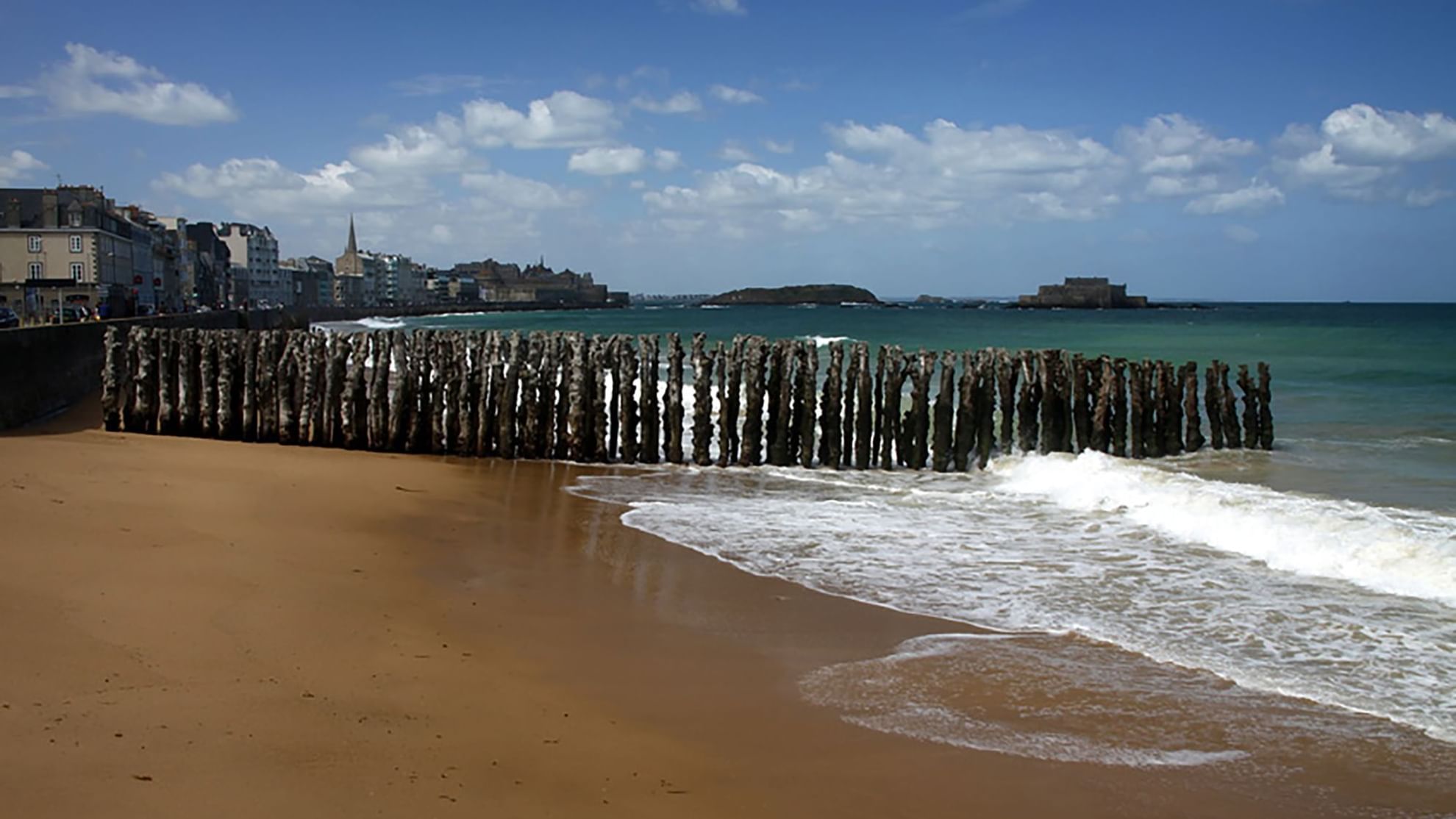 Sandy beach with wooden posts emerging from the waves featuring Saint Malo Beach near Warwick Hotels and Resorts