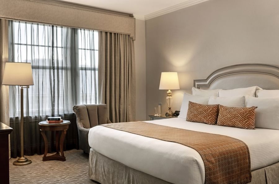 King bed with patterned pillows by a wooden side table under a glowing lamp in Traditional King at Warwick Melrose Dallas
