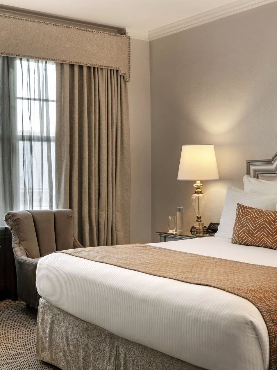 King bed with brown and white pillows and a flower vase on the nightstand at Warwick Melrose Dallas.