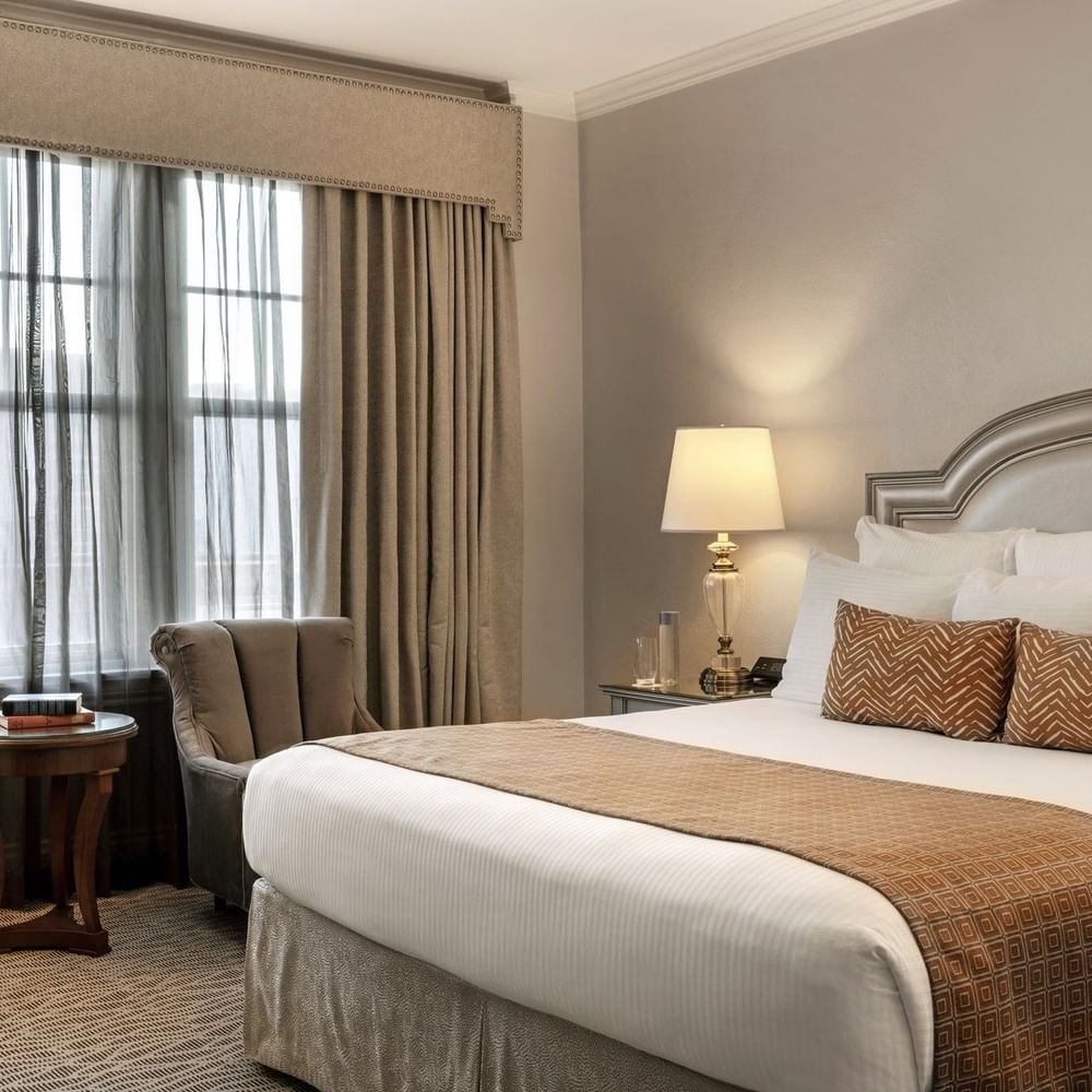 King bed with brown and white pillows and a flower vase on the nightstand at Warwick Melrose Dallas.