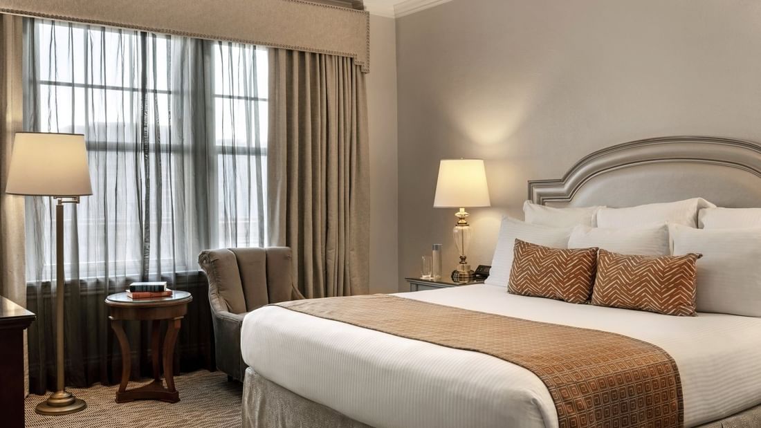 King bed with patterned pillows by a wooden side table under a glowing lamp in Traditional King at Warwick Melrose Dallas