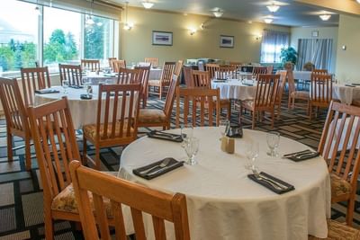 Round tables with white linens & wooden chairs placed beneath bright lights in The Okanagan at Hilltop Inn Salmon Arm