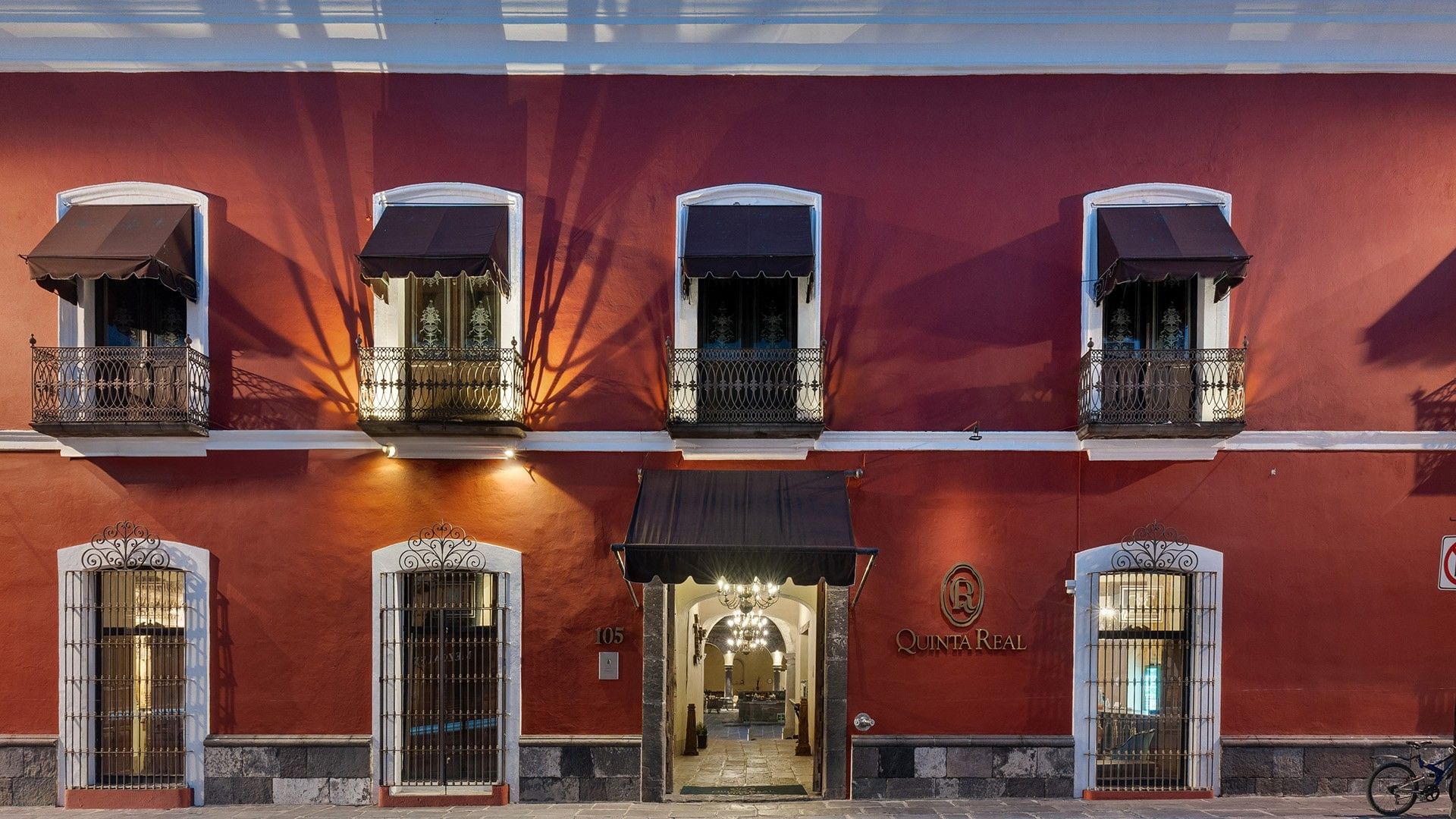 Exterior view of Quinta Real Puebla hotel with red walls, black awnings, and wrought iron balconies