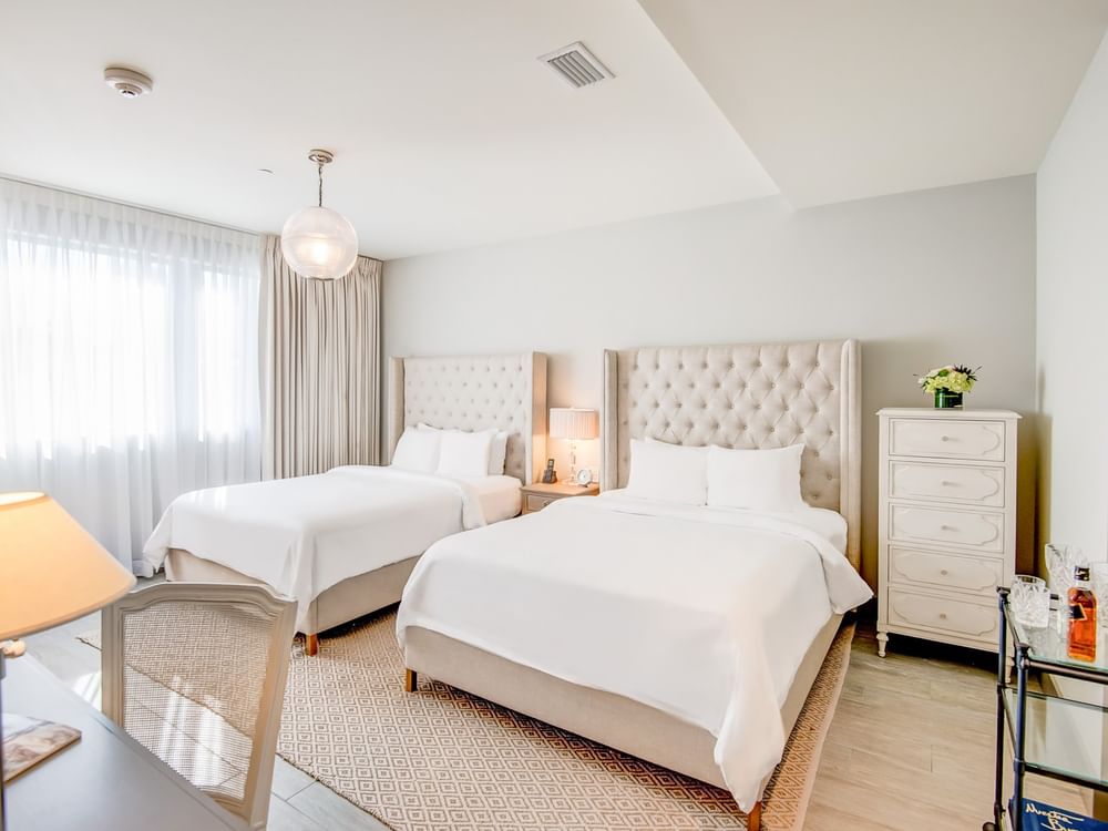 A hotel room with two beds, tufted headboards, and white linens.