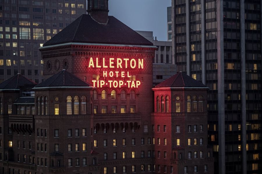 Exterior of the Warwick Allerton Chicago with a glowing sign near city skyscrapers