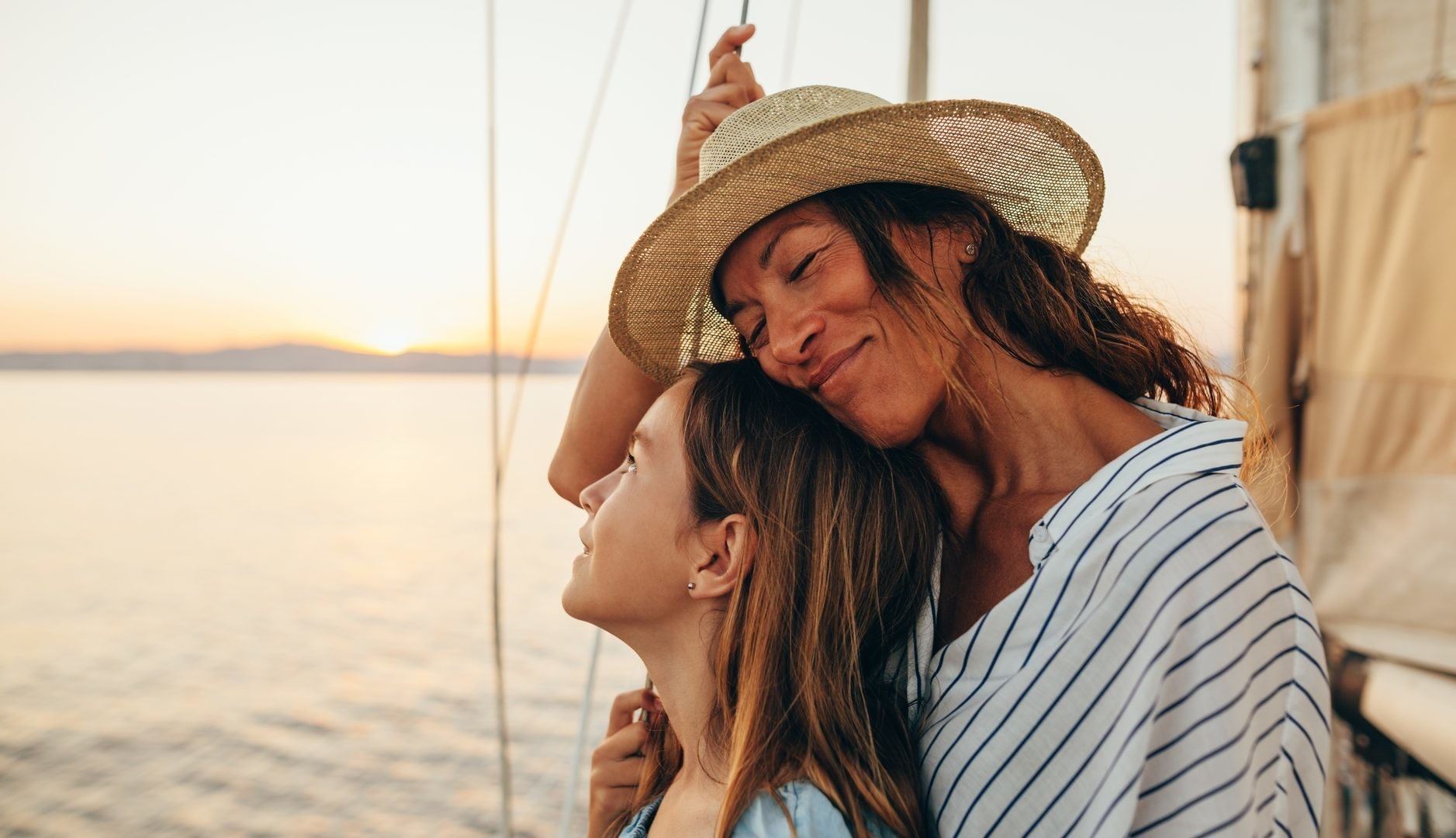 Woman in straw hat and striped shirt embracing another person on a sailboat at sunset at Falkensteiner Resort Lake Garda
