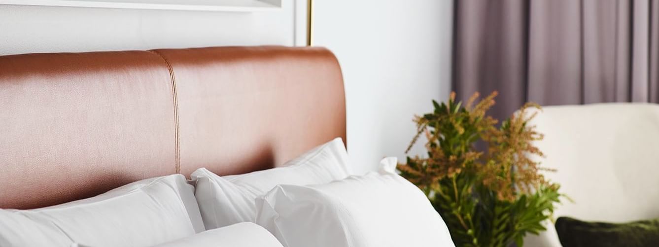 Pillows against tan leather headboard with modern reading lamp in Accessible Room at Novotel Sydney Darling Square
