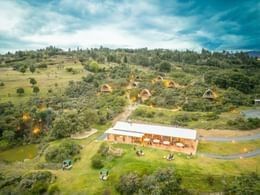 Aerial view of glamping cabins among lush green trees behind a dining pavilion in the scenic countryside at Unika Hotels