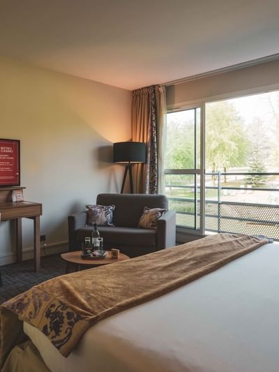 Chambre d'hôtel avec lit, bureau, télévision, fauteuil, table basse et balcon vitré.