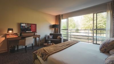 Hotel room with a large bed, desk, TV, with outdoor view.