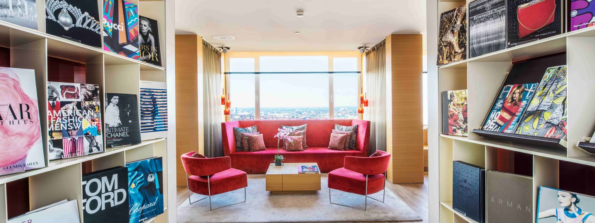 Lounge featuring red sofa and armchairs by the windows with panoramic city view at The Hotels Brussels
