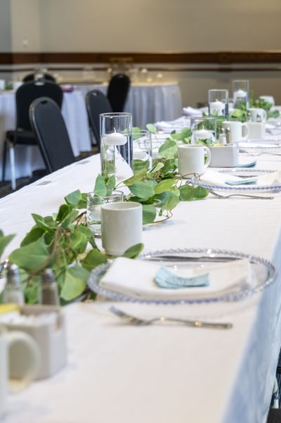 Long banquet table decorated with green leaves by white candles under dim lights at Rodd Brudenell River Resort