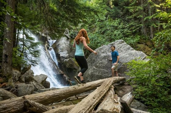 A woman and a man hiking on a trail by a waterfall at Aava Whistler.