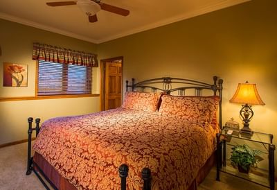 A traditional bedroom at The Stanley Hotel with a large bed, a red comforter, and a ceiling fan with lights
