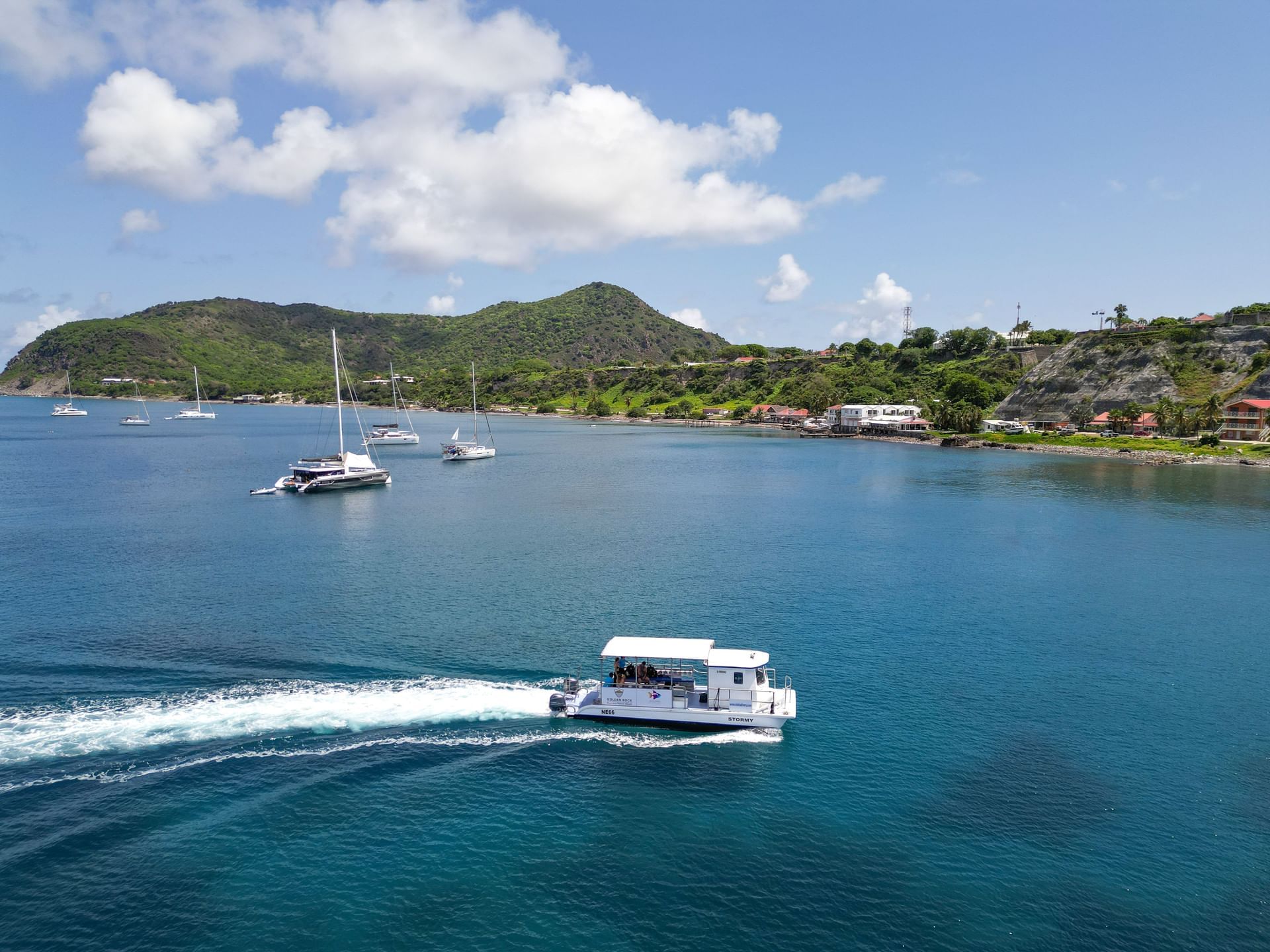 Boat cruising through clear blue waters near lush green hills in Sint Eustatius harbor near Golden Rock Resort