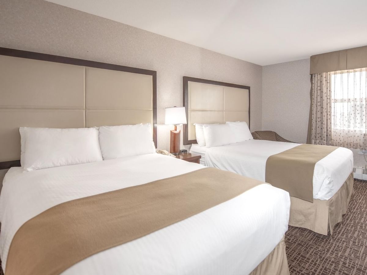 Two beds, a lamp, and a chair near a window.