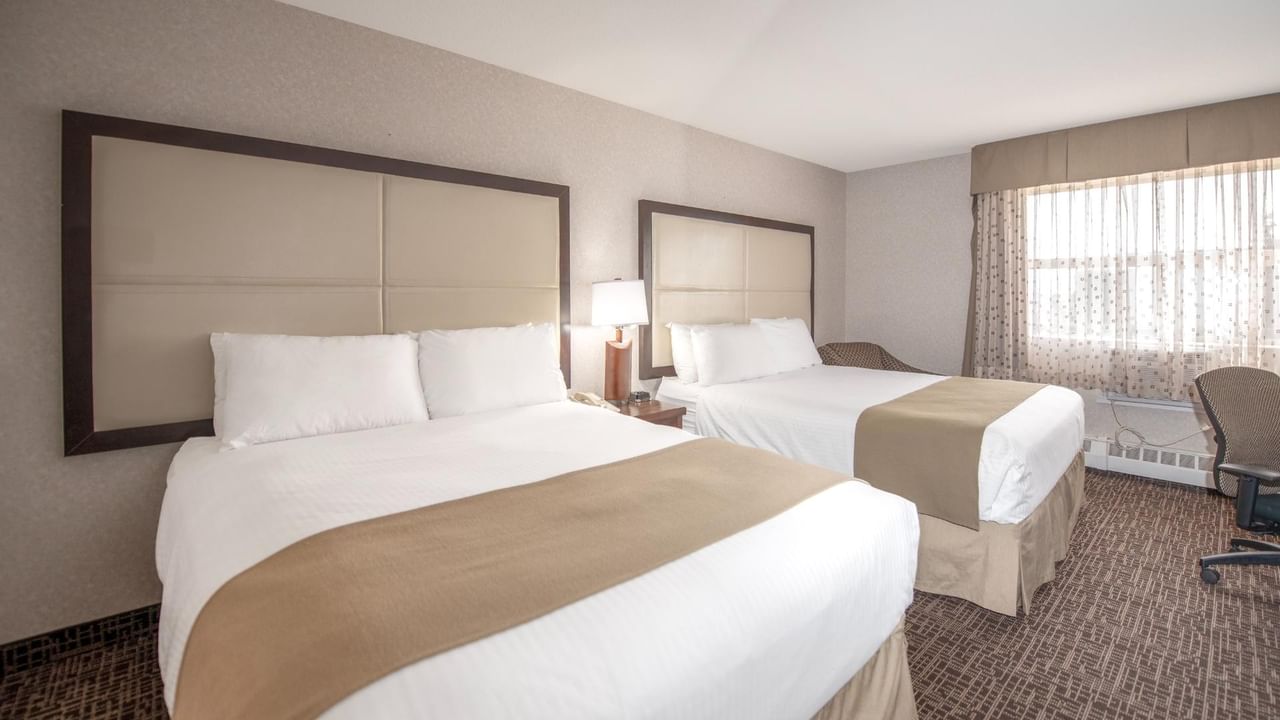 Two beds, a lamp, and a chair near a window.