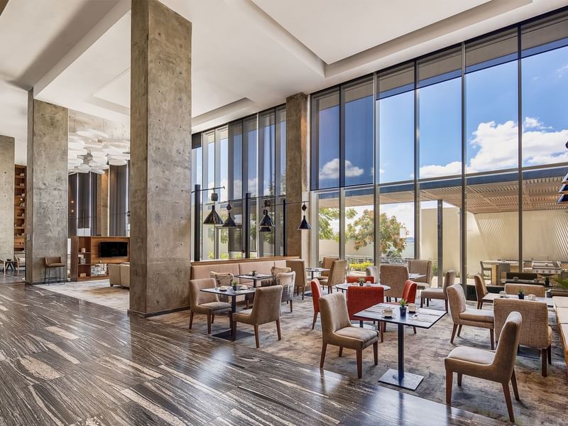 Restaurant with dining tables, comfy chairs and large windows with garden view at Fiesta InFiesta Inn Suites Aeropuerto del Bajío Silao