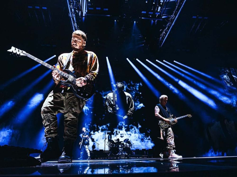 Avenged Sevenfold performing on stage with guitars and blue lights at a concert.