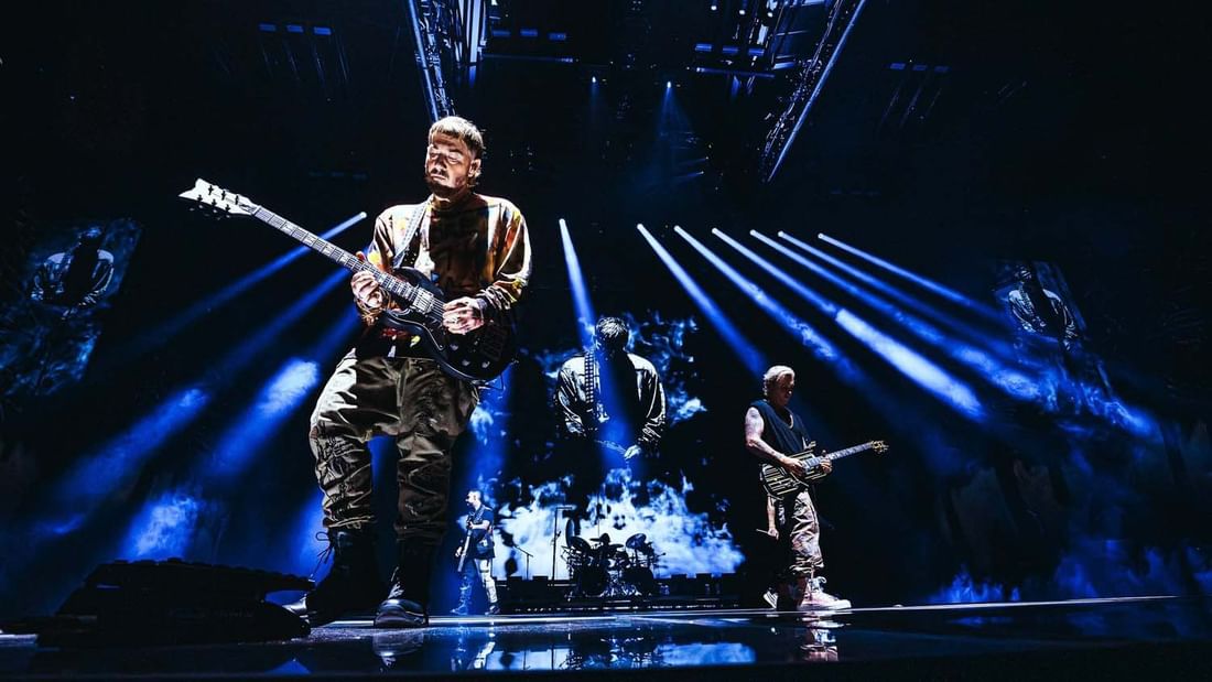 Avenged Sevenfold performing on stage with guitars and blue lights at a concert.
