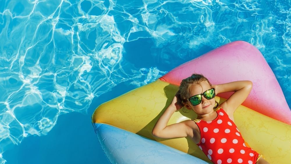 Young girl wearing sunglasses relaxing on a colorful inflatable raft in a clear swimming pool at Rosen Inn International