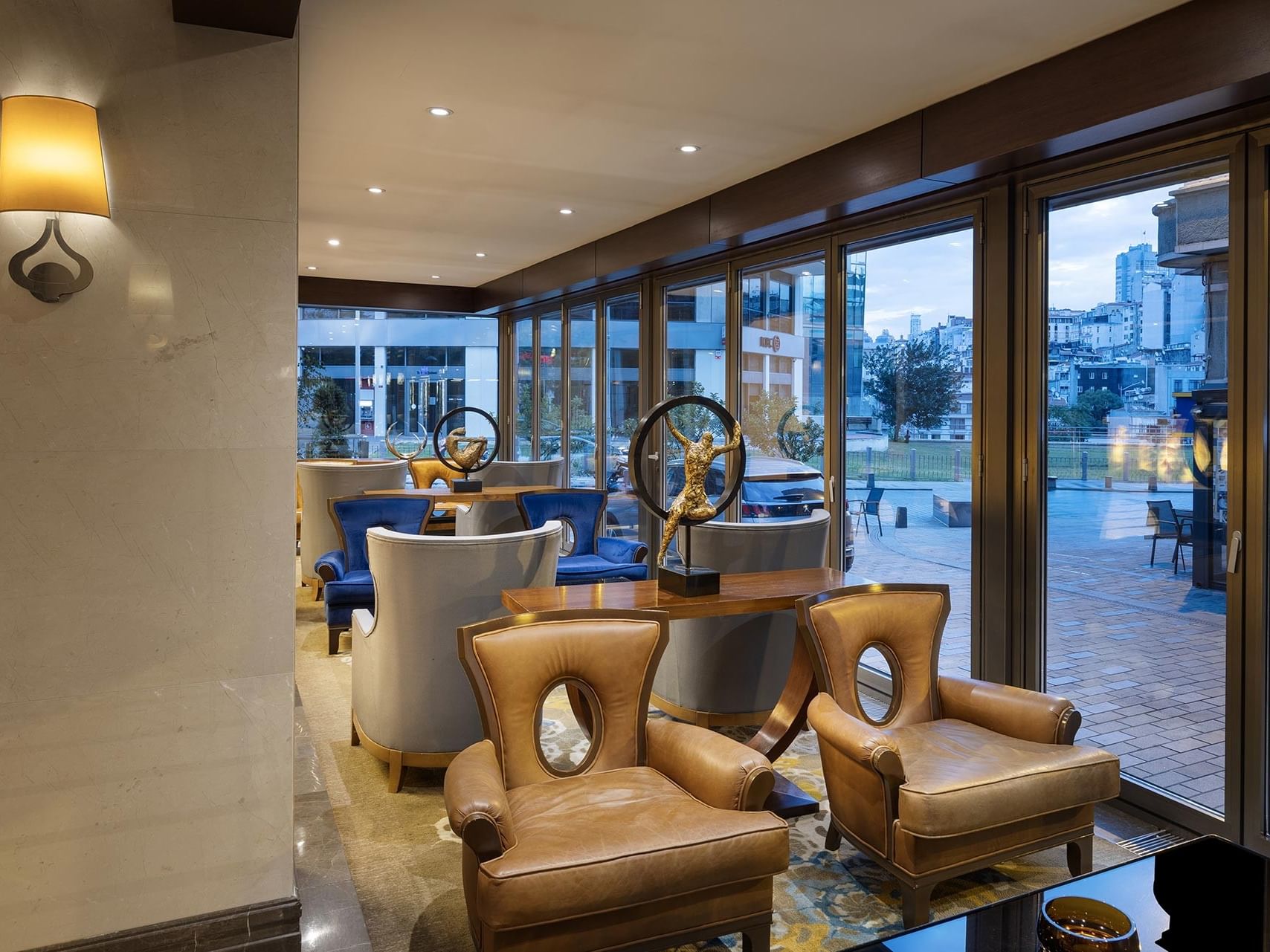 Titanic City Taksim lobby area with brown leather chairs, a table, and windows showing cityscape.