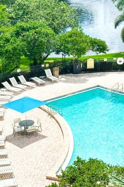 A shot of a clear pool surrounded by lounge chairs with green trees and a small lake in the distance at Rosen Inn Lake Buena Vista.