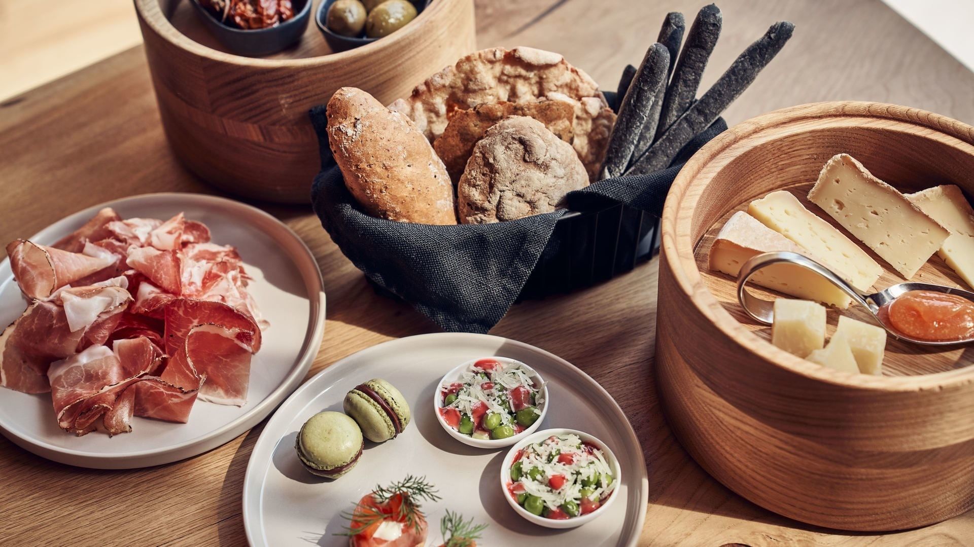 Varie prelibatezze su piatti e in ciotole, tra cui salumi, formaggi e verdure, disposti su un tavolo in legno.