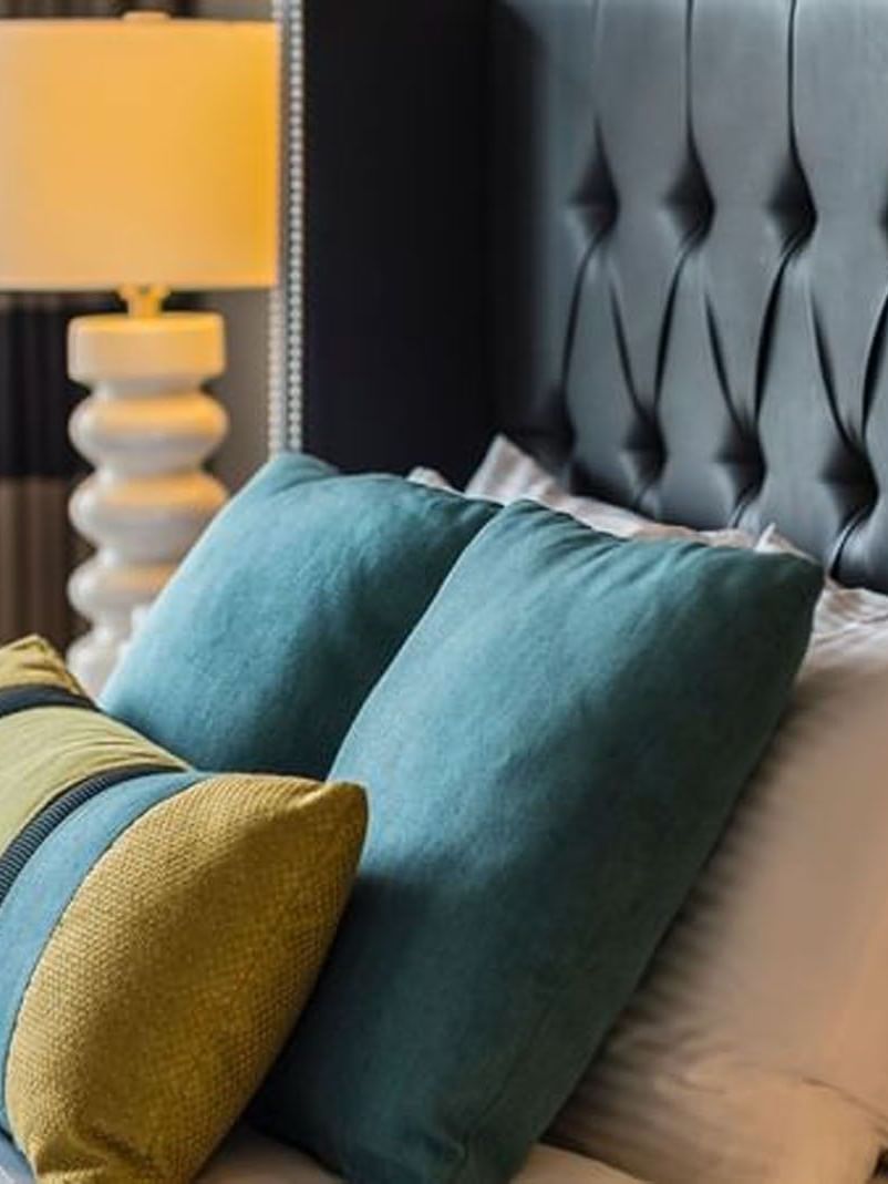 Teal and yellow pillows by a white lamp under a tufted black headboard in Emerald Suite at Warwick Seattle